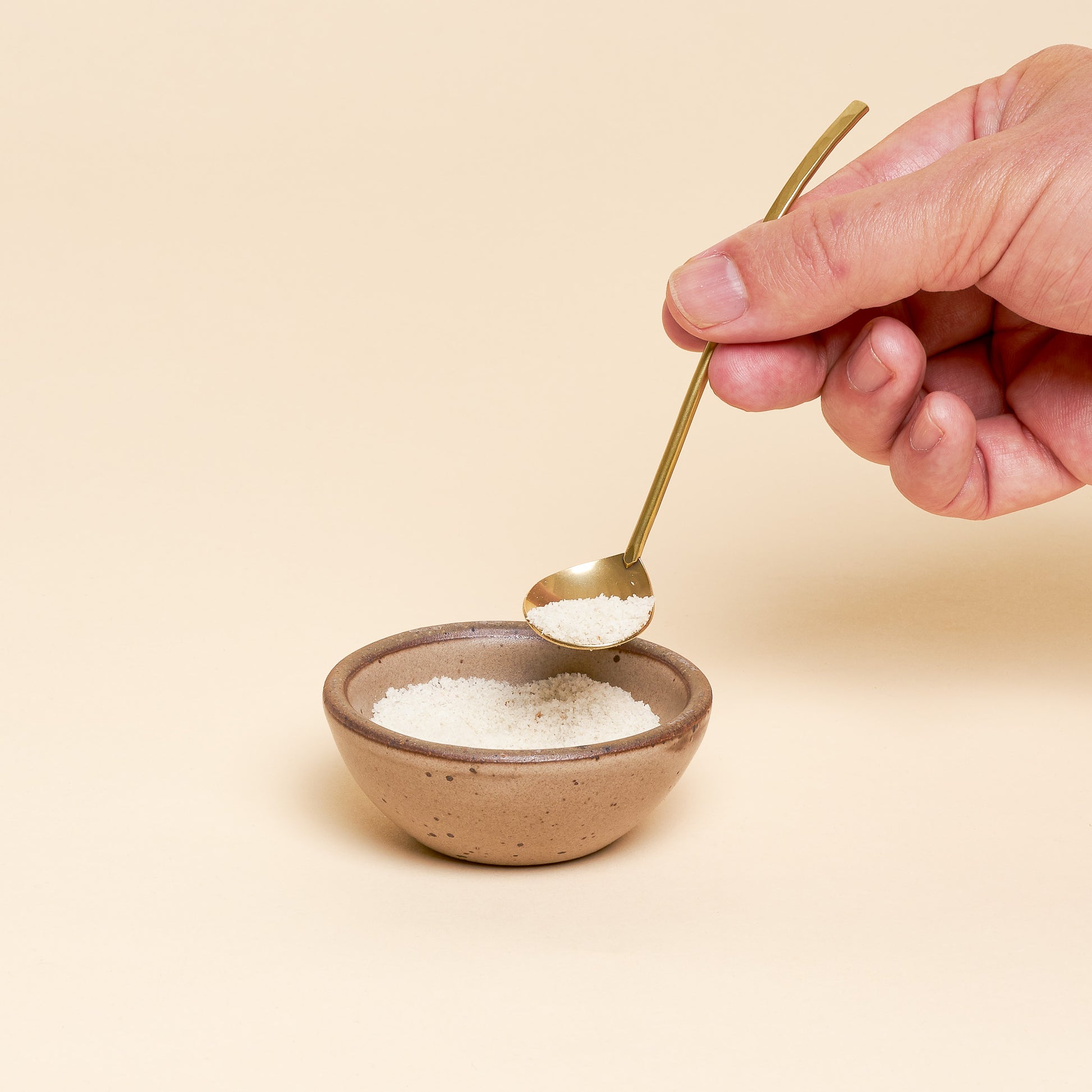 A hand holds a miniature ladle over an East Fork Bitty Bowl with a pinch resting in its spoon.