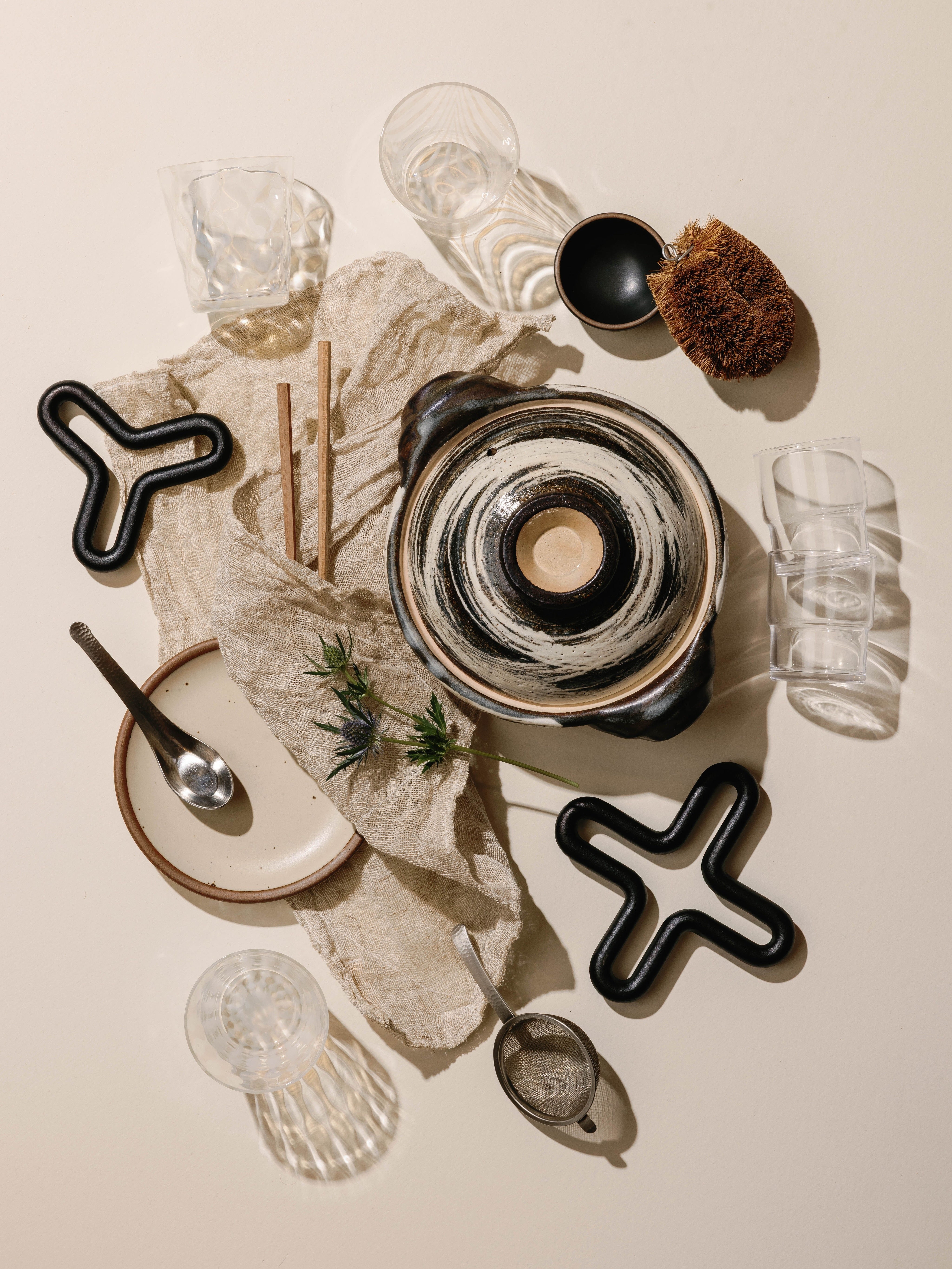 An overhead of donabe, glassware, trivets and linens on a cream background