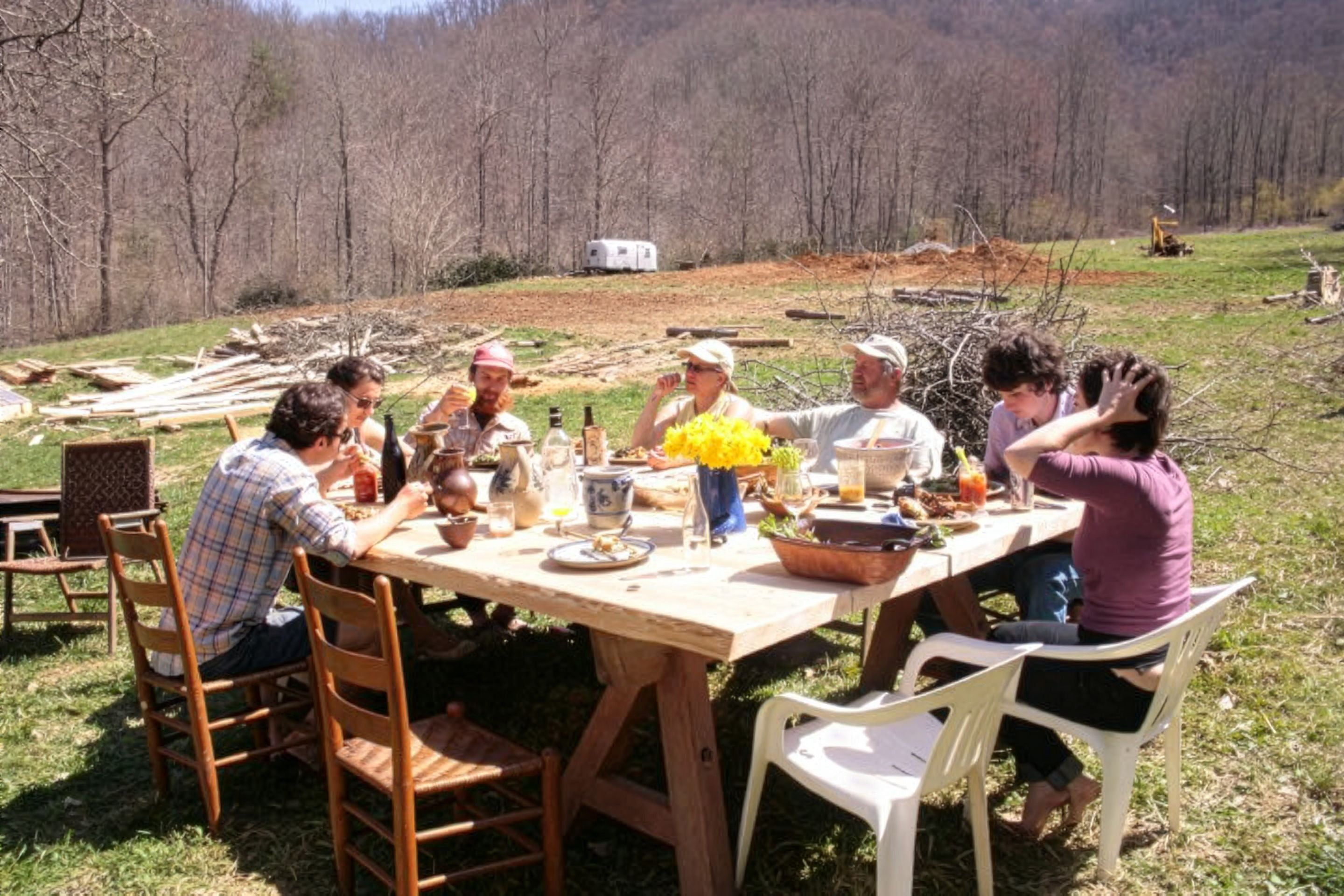A group of people sit around a table eating lunch outside in the sun