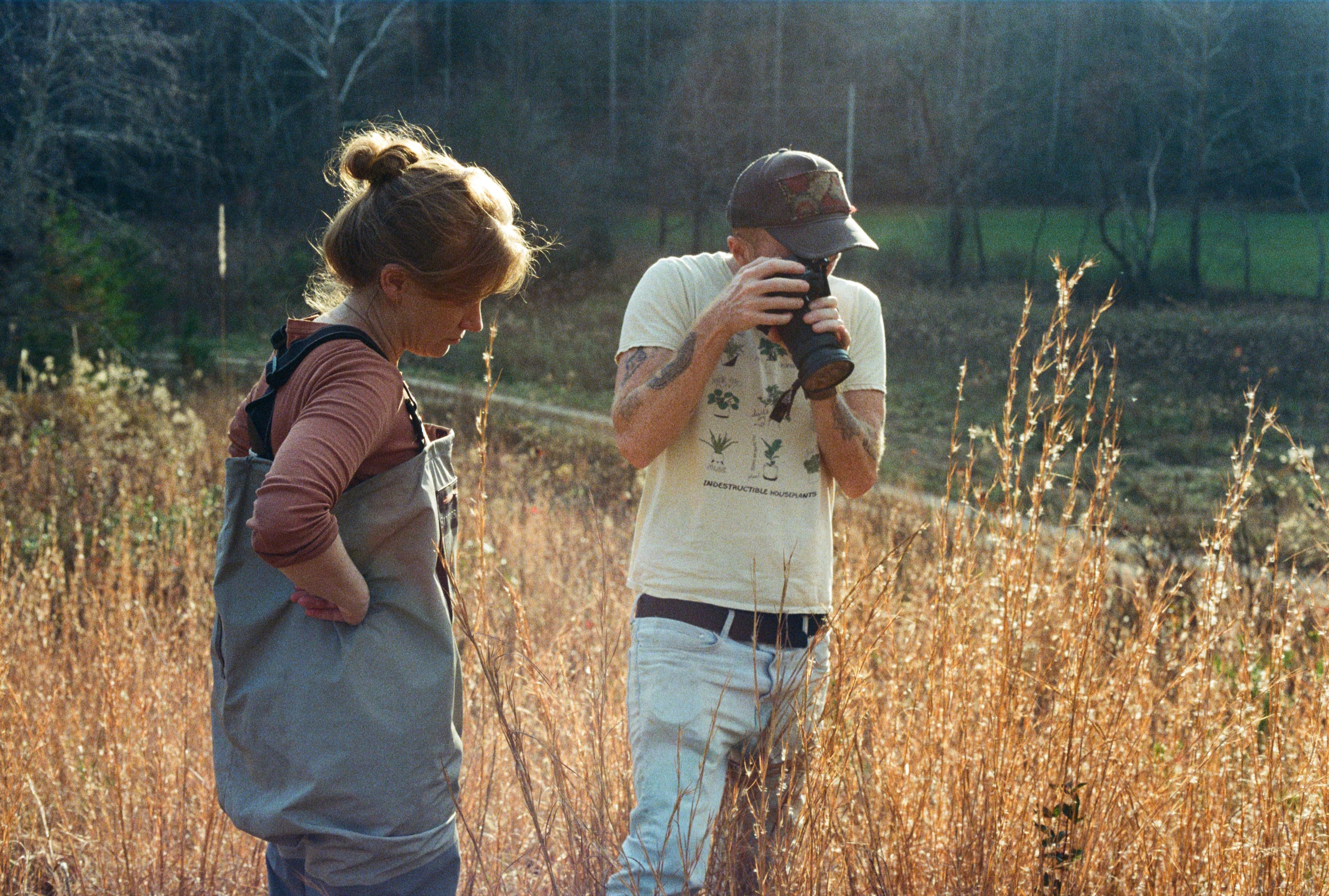 A man and a woman standing in a field of tall grass taking photos